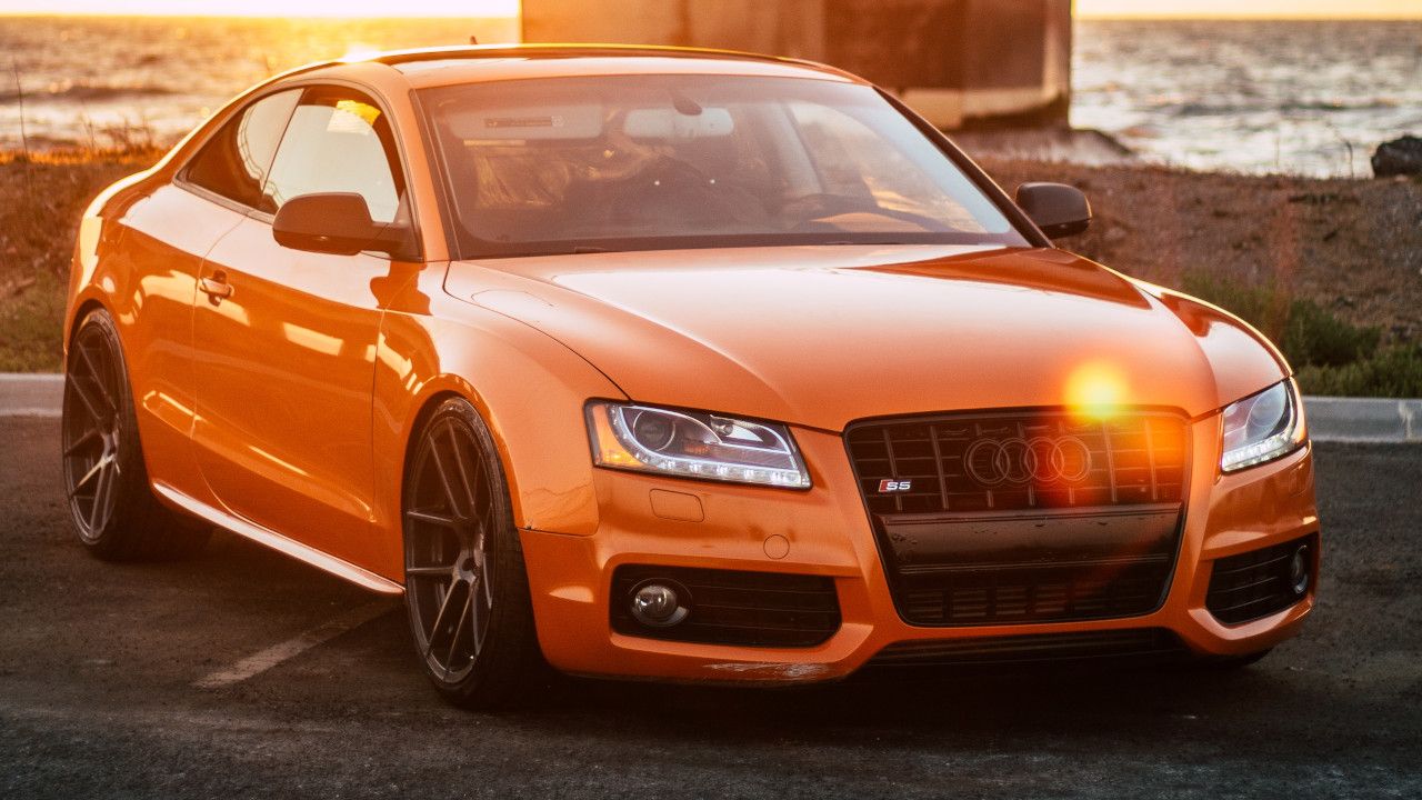 Orangener Audi steht auf einem Parkplatz bei Sonnenuntergang